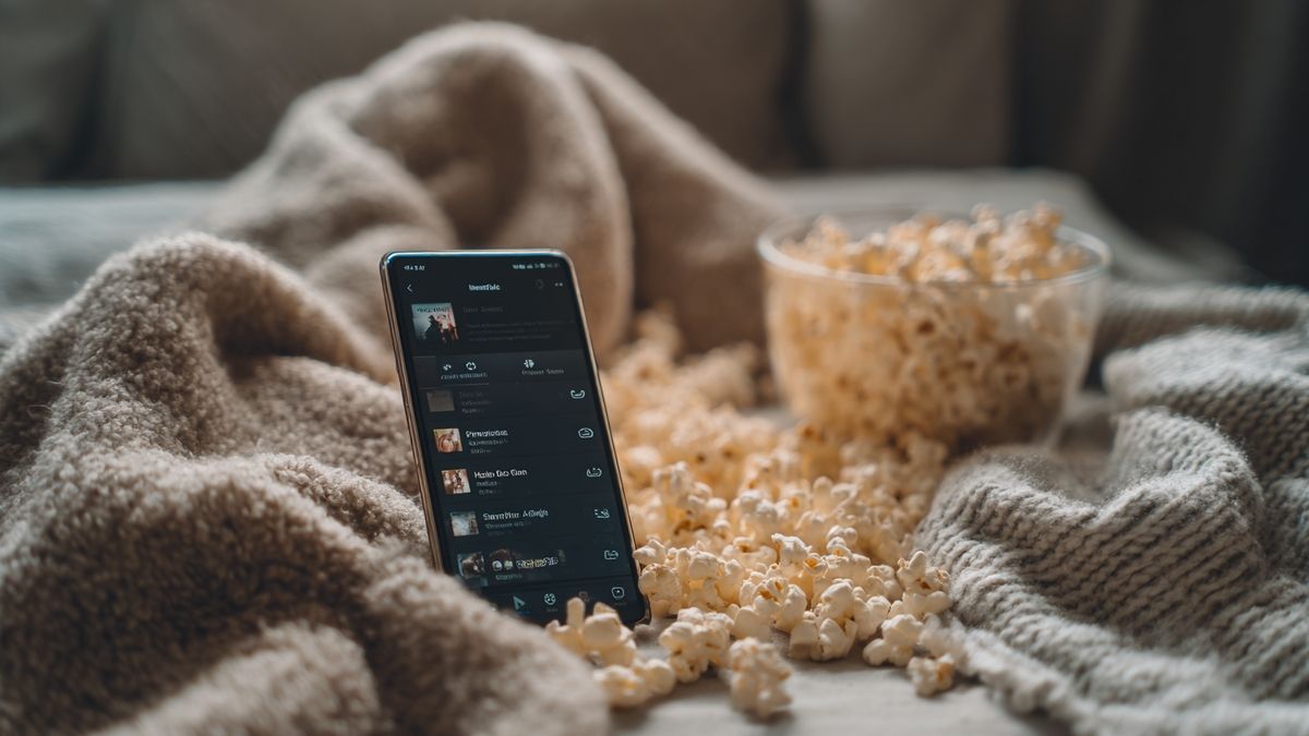 A close-up view of a smartphone showcasing Dopriv streaming services with surrounding popcorn and comfy blankets.